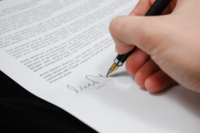 Una mano con una pluma, firmando un documento